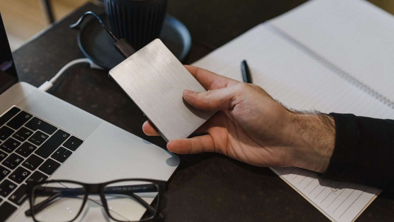 Hard disk extern conectat la un laptop deschis pe un birou, în timpul copierii fotografiilor