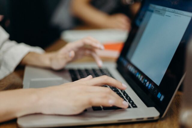 Persoană care scrie la laptop într-un birou luminos, cu notițe și un telefon pe masă